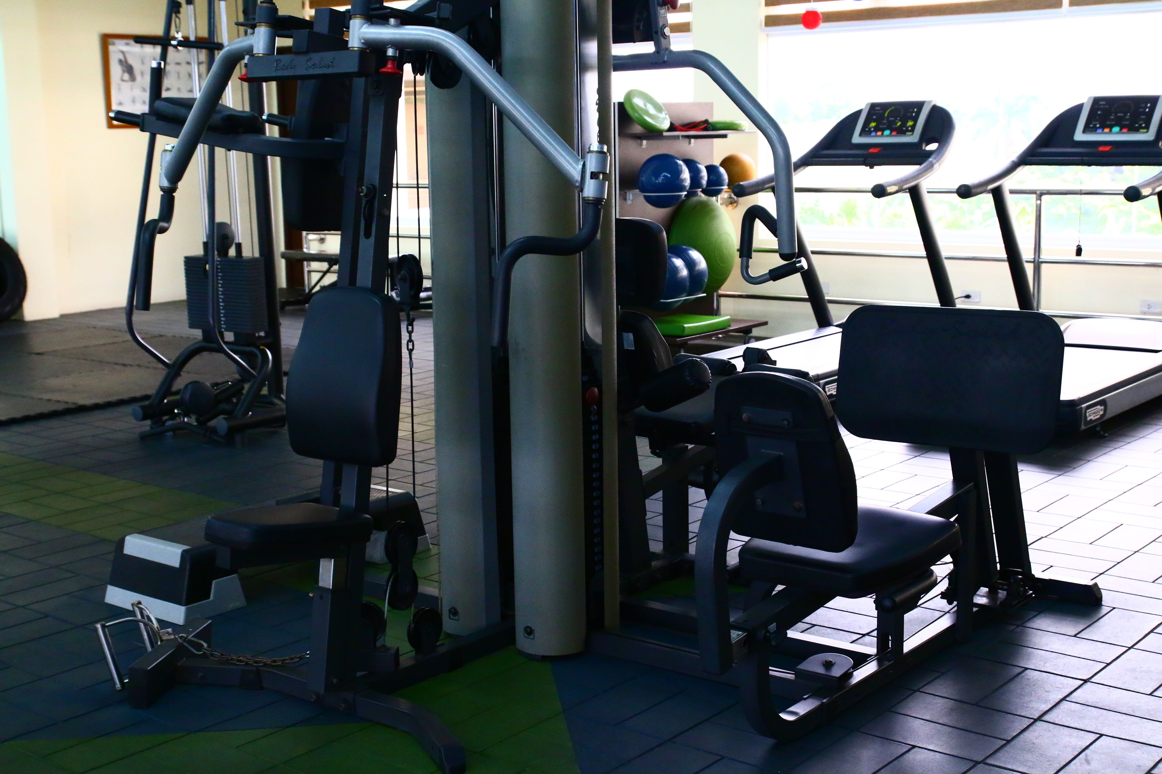 Ein Fitnessstudio mit Trainingsgeräten, Laufbändern und einem Bereich mit grünen Matten.