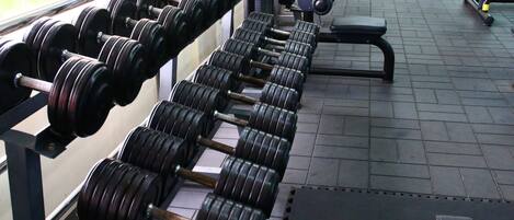 Un gimnasio con filas de mancuernas y discos de pesas, una banca y una pesa rusa.