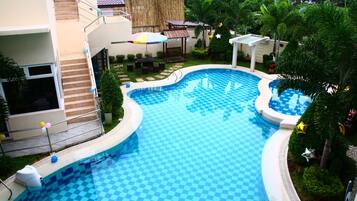 Una piscina con diseño de cuadros, rodeada de follaje y un edificio con balcón.