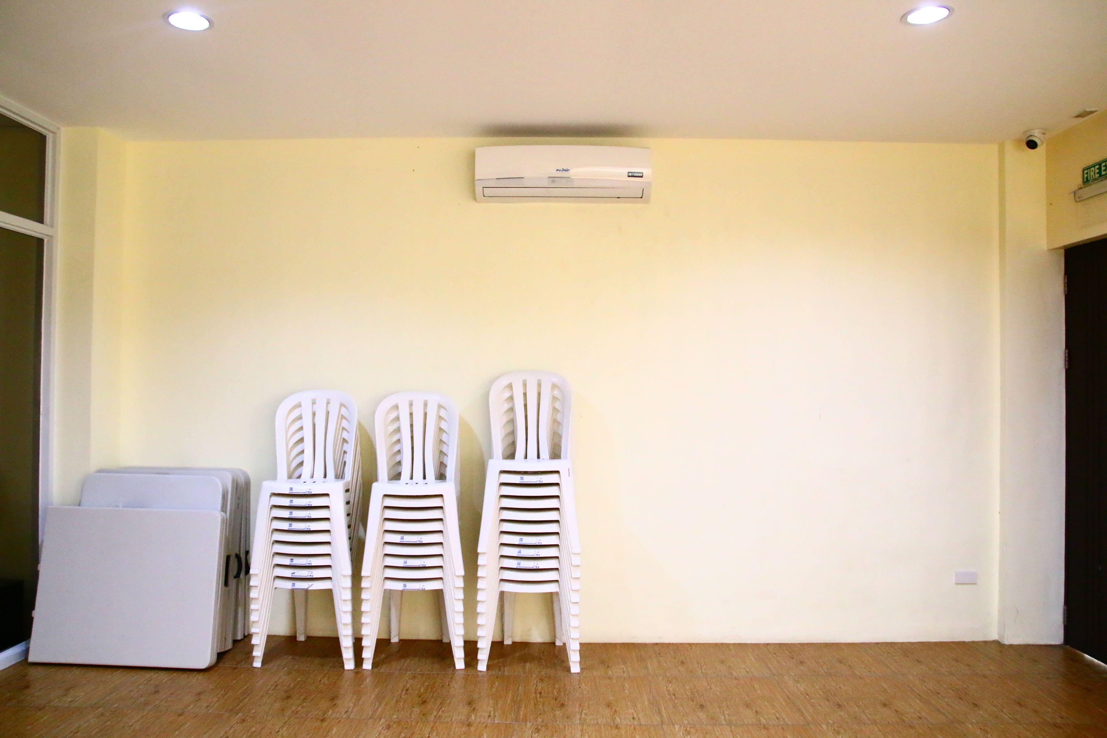 Una habitación con un aire acondicionado blanco, una pila de sillas de plástico blancas y un armario blanco.