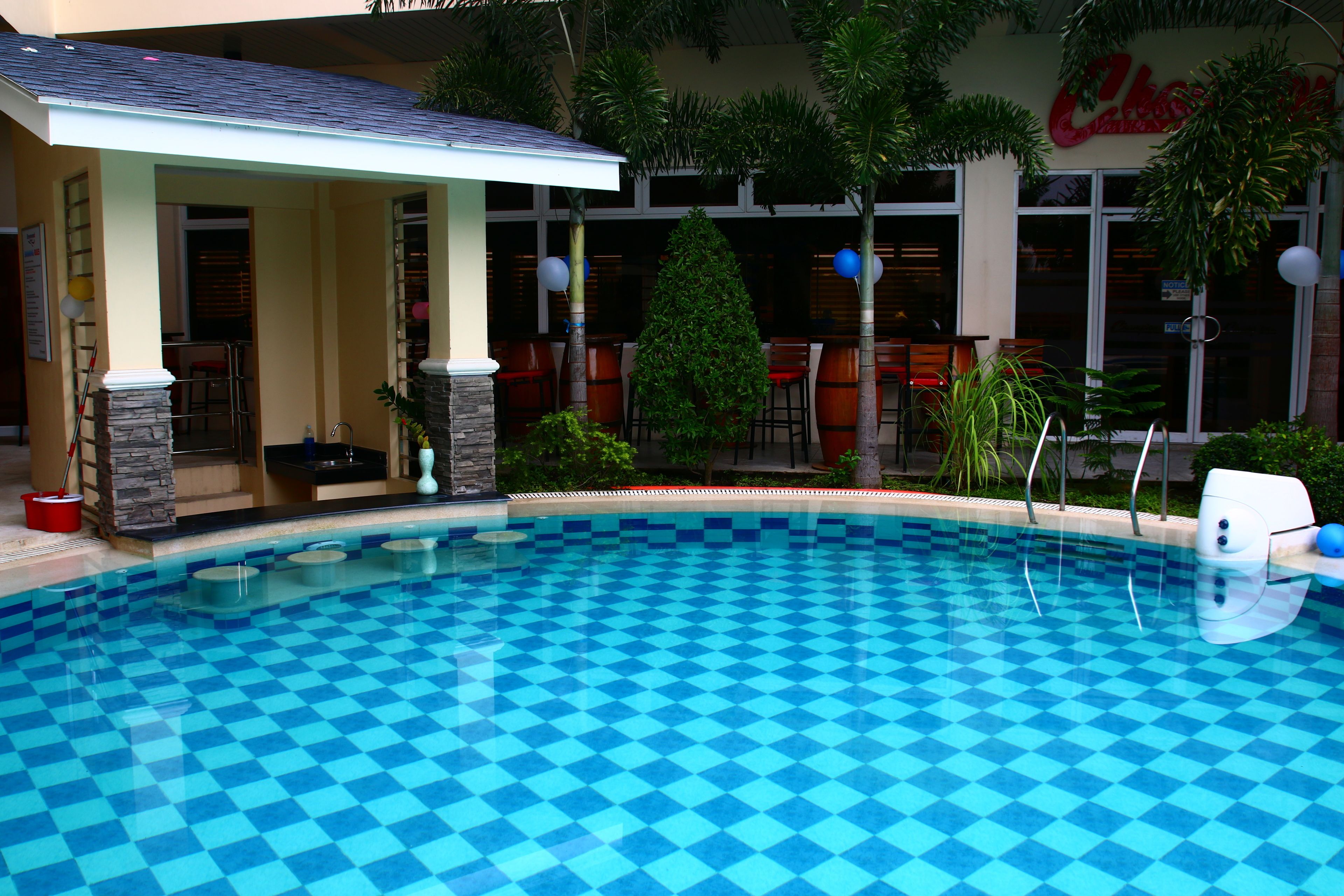 A pool with a checkered pattern, a covered seating area, and a restaurant in the background.