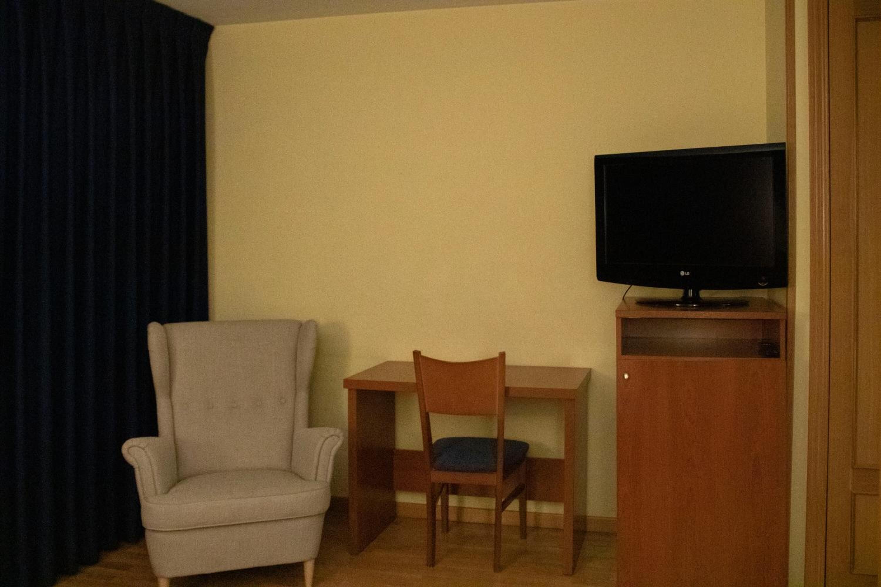 Une pièce comprenant une seule chaise, une petite table et un téléviseur posé sur un meuble.