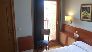 Een hotelkamer met een bed, een stoel, een bureau, een lamp en een schilderij aan de muur.
