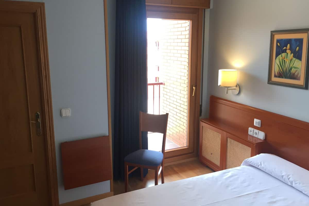 Ein Hotelzimmer mit einem Bett, einem Sessel, einem Schreibtisch, einer Lampe und einem Bild an der Wand.