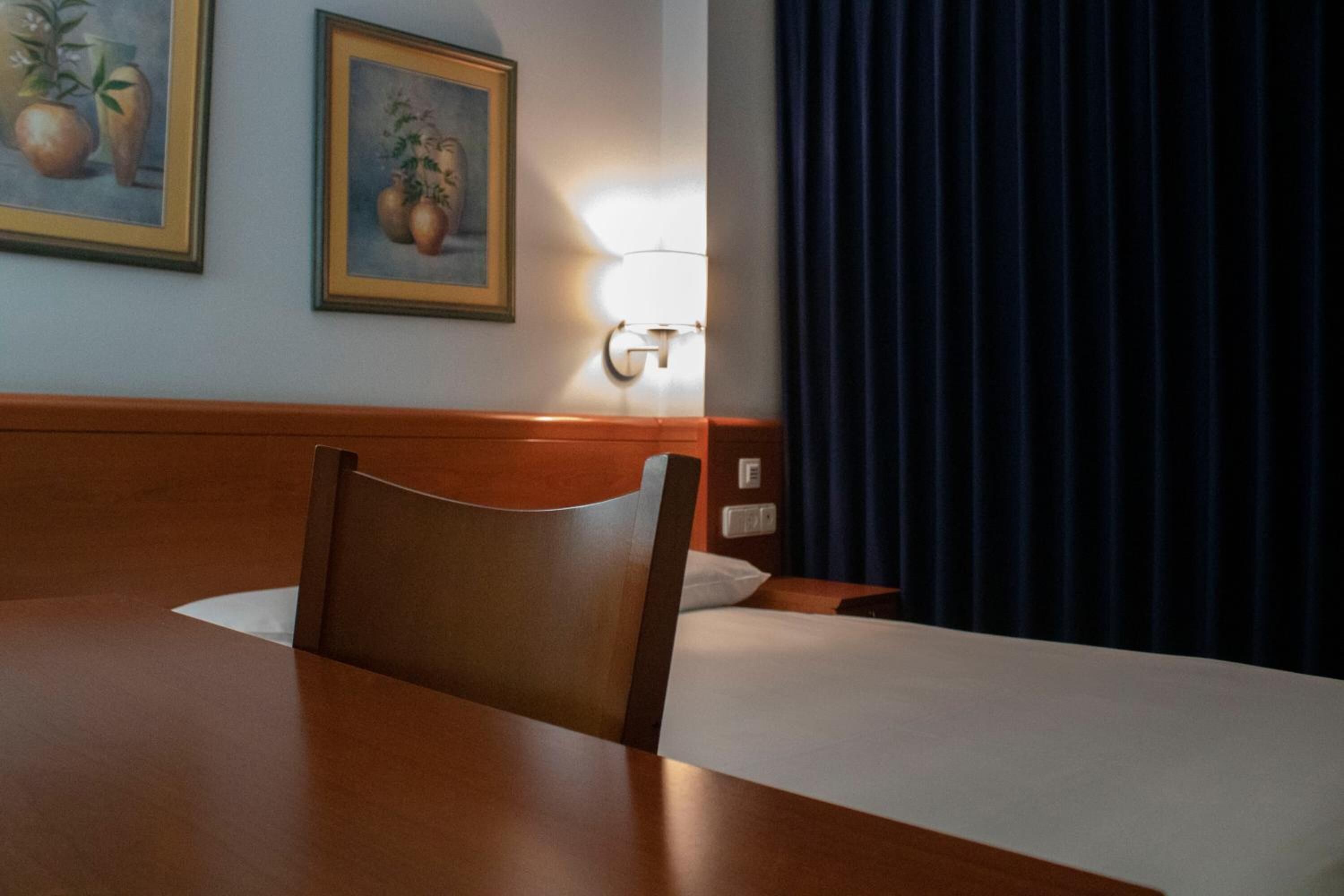 A hotel room with a wooden headboard, a bed with white linens, a table, and two framed paintings on the wall.