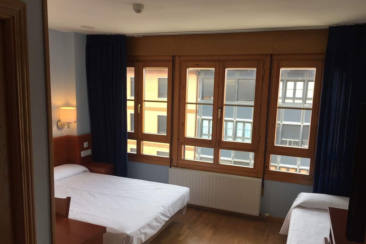 Ein Hotelzimmer mit zwei Betten, Holzböden, einem Heizkörper und großen Fenstern mit Vorhängen.