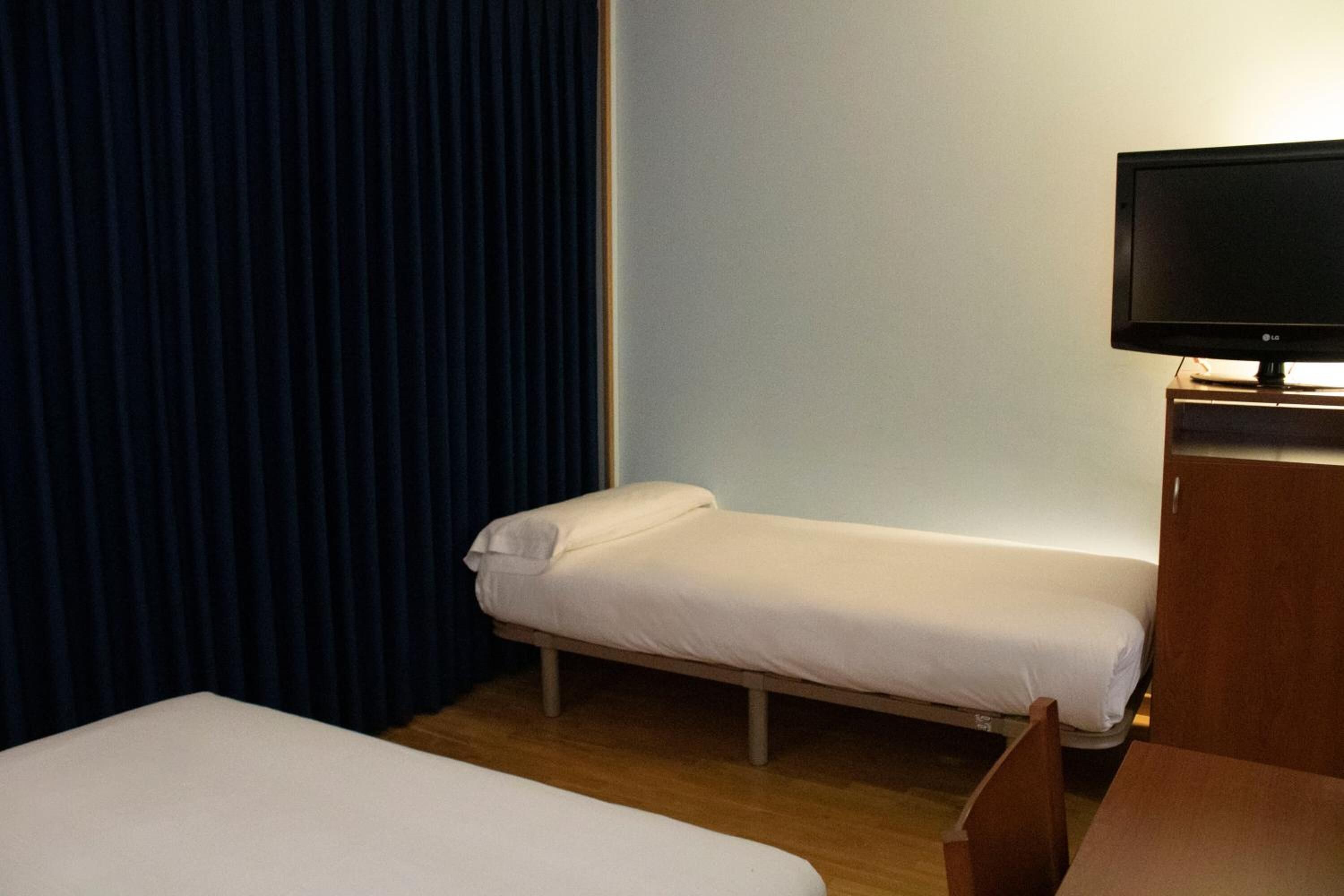 Une chambre d’hôtel avec un lit simple, un petit bureau et un téléviseur.