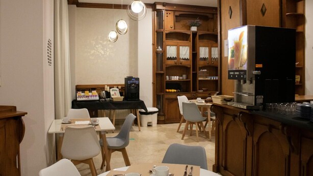 Een eethoek met tafels, stoelen, een koffieapparaat en een koelkast.