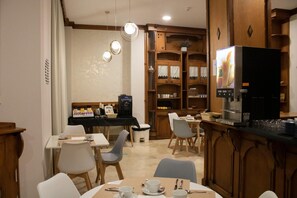 Un comedor con mesas y sillas, una cafetera y un refrigerador.
