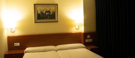 A hotel room with a double bed, two bedside tables, a wall-mounted light, and a painting.