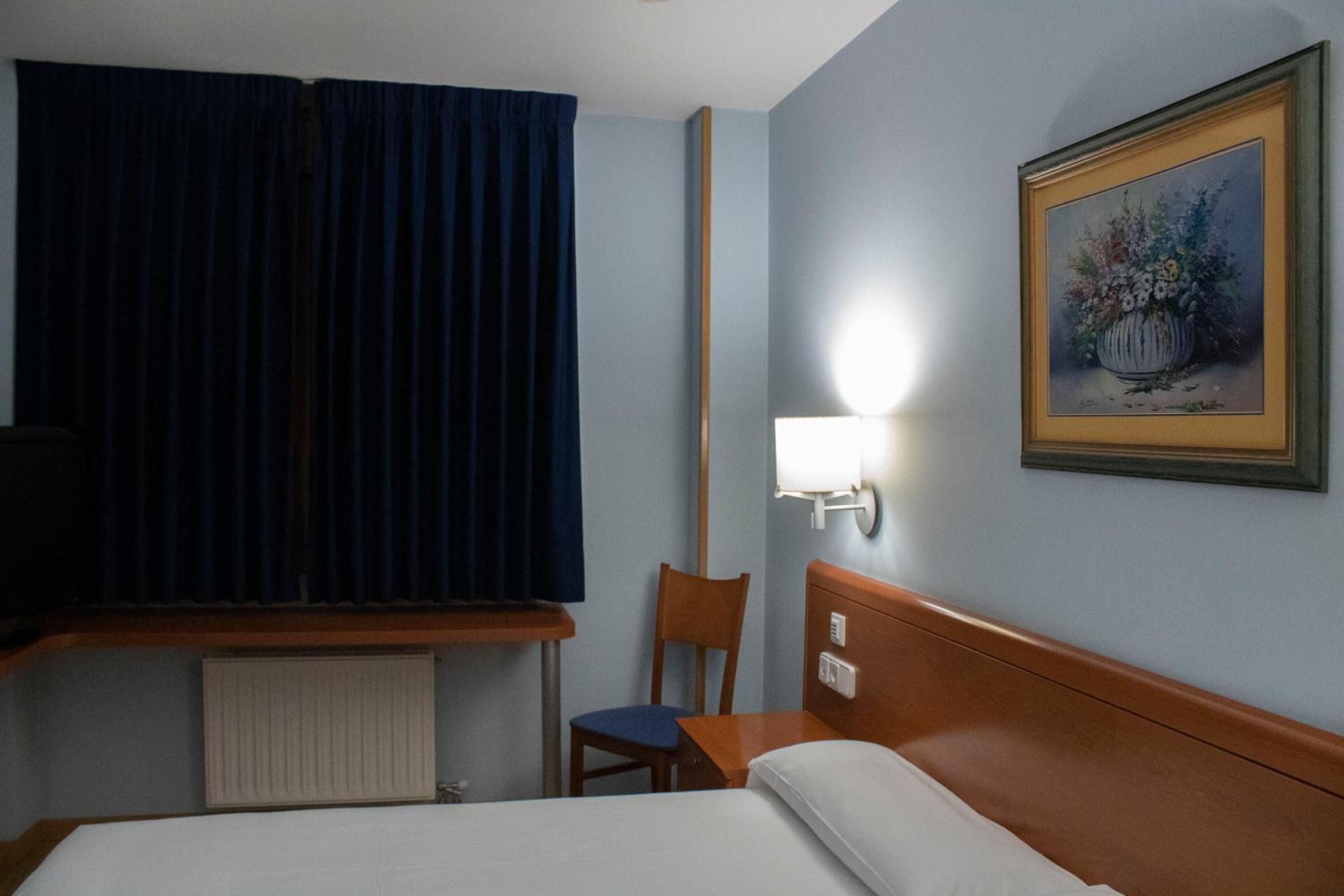 Habitación de hotel con cama, una silla, un escritorio, una lámpara y un cuadro en la pared.