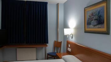 Habitación de hotel con cama, una silla, un escritorio, una lámpara y un cuadro en la pared.