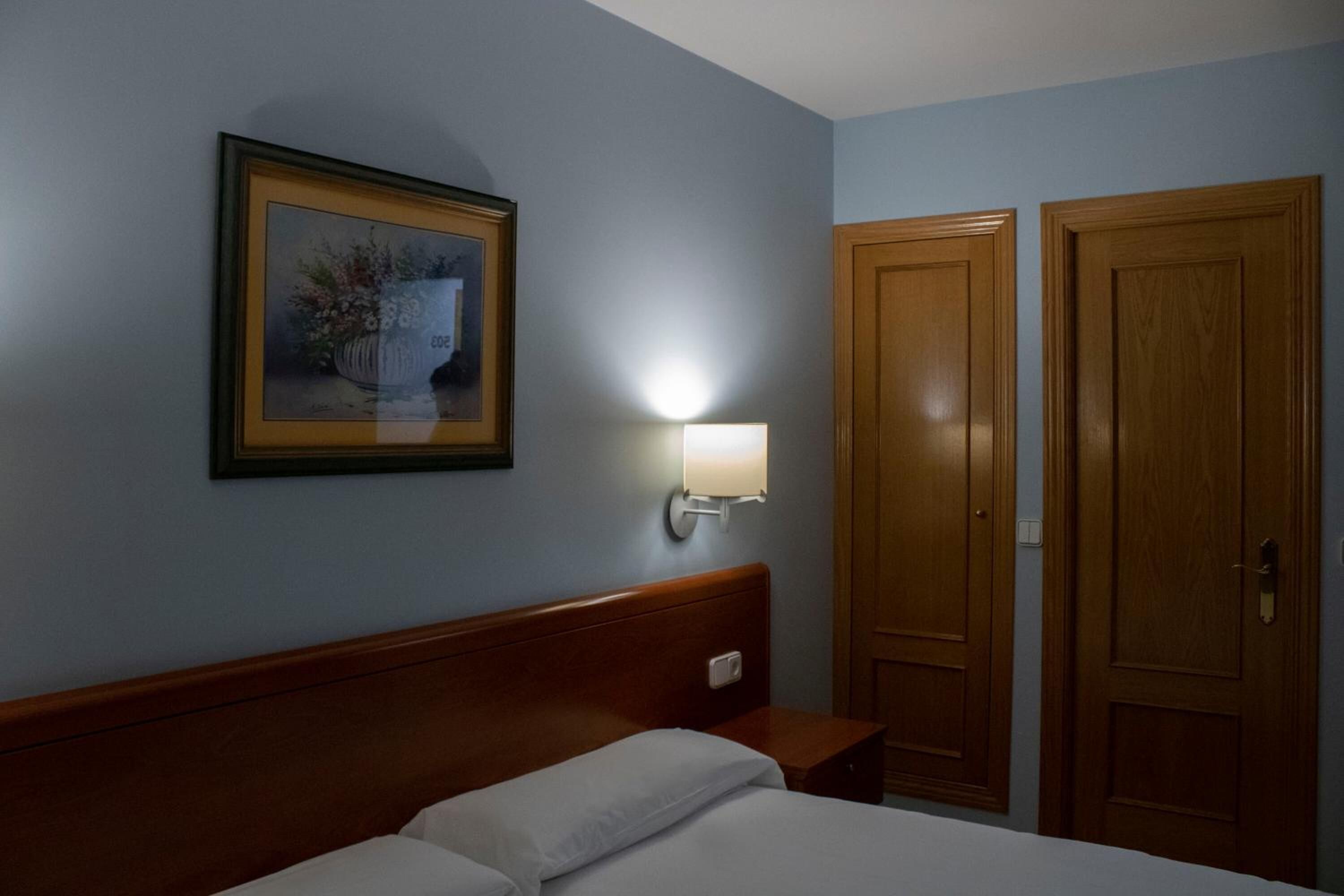 Een hotelkamer met een bed, een nachtkastje, een wandlamp en twee houten deuren.