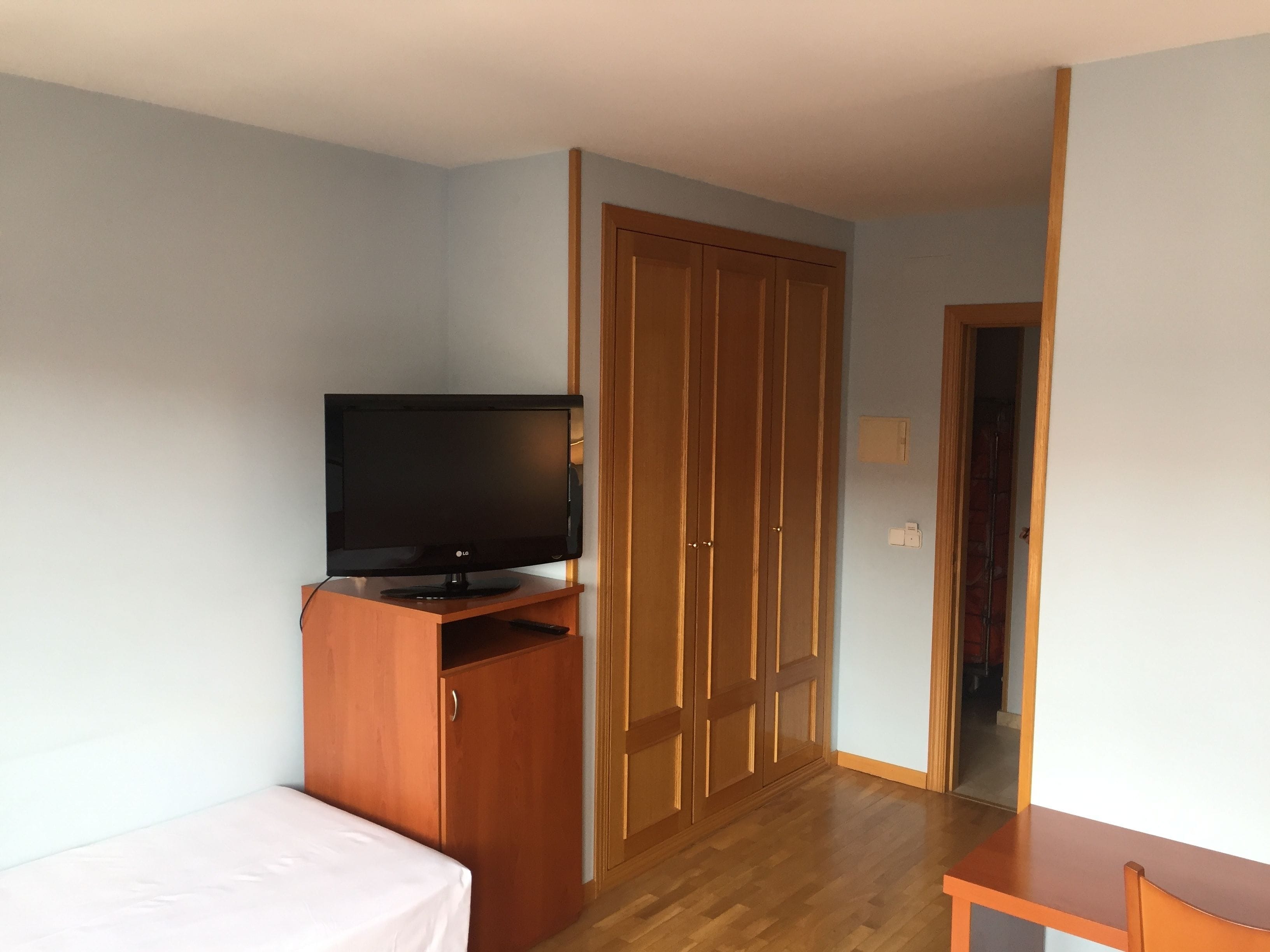 Una habitación con una cama, un televisor sobre un mueble de madera, un armario y una pequeña mesa.