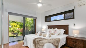 A bedroom with a bed, bedside lamps, a nightstand, and a view of a balcony with outdoor furniture. - Tropical 3 Bedroom House, Pool plus 4th Bedroom Bungalow (Whitfield)