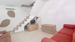 Een woonkamer met een trap, een rode bank, een televisie en een klein tafeltje.