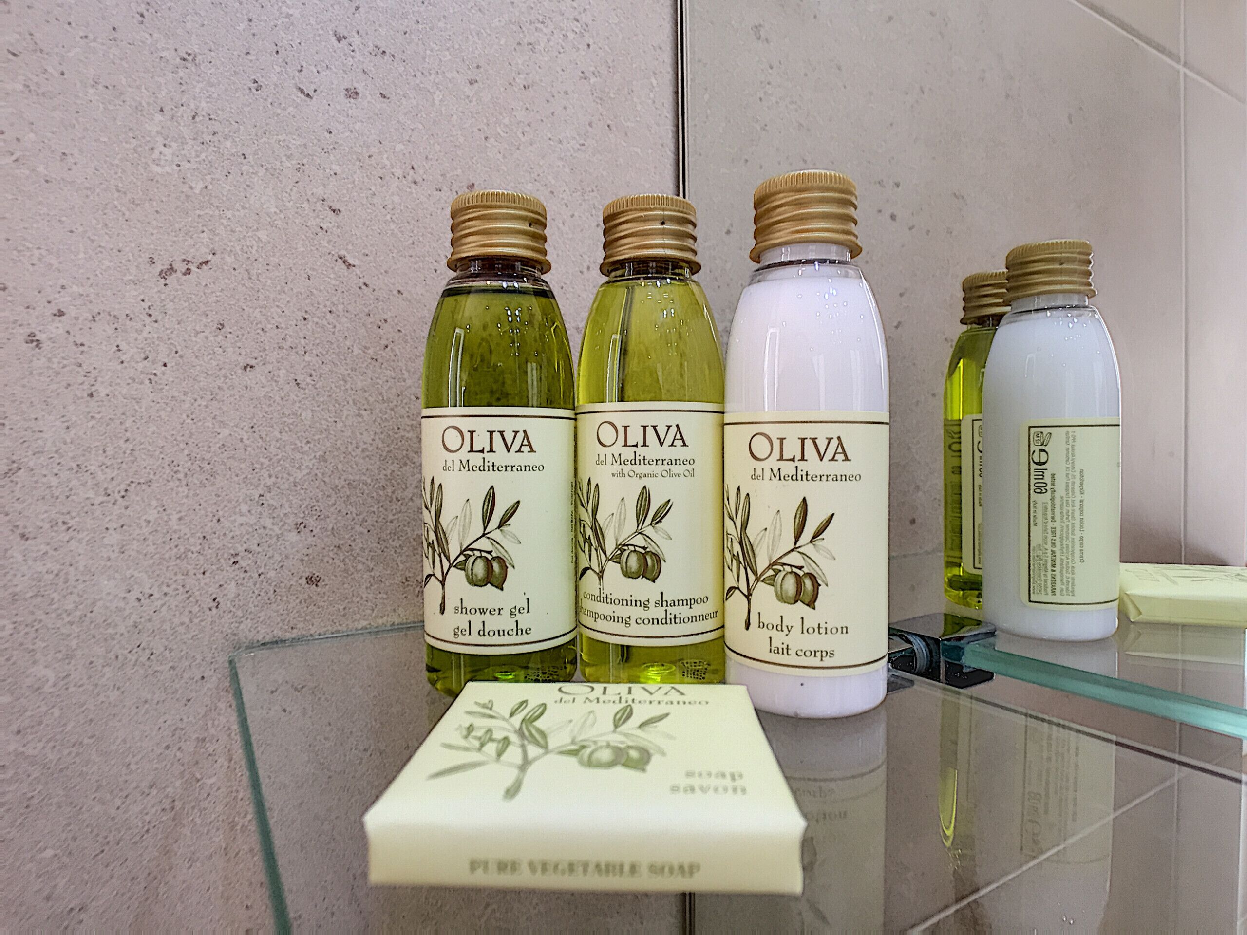 A bathroom shelf with three bottles of olive-based products and a bar of soap.