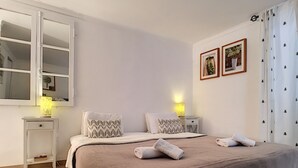 Een netjes ingerichte slaapkamer met een groot bed, twee nachtkastjes met lampen, een spiegel en twee ingelijste foto’s aan de muur.
