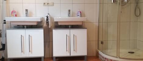 Ein Badezimmer mit zwei Waschbecken, einem Spiegel, einer Dusche und einem Fliesenboden.