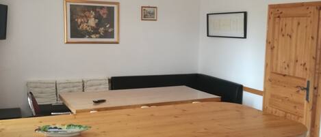 A dining area with a wooden table, chairs, and a bench. There are hanging lights and framed pictures on the wall.