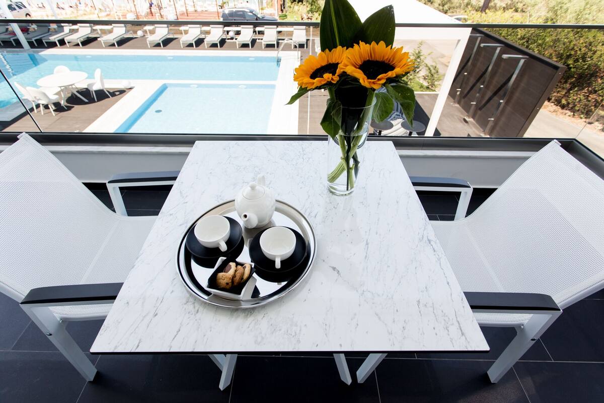 A terrace with a table set for tea, a vase with sunflowers, and a pool in the background.