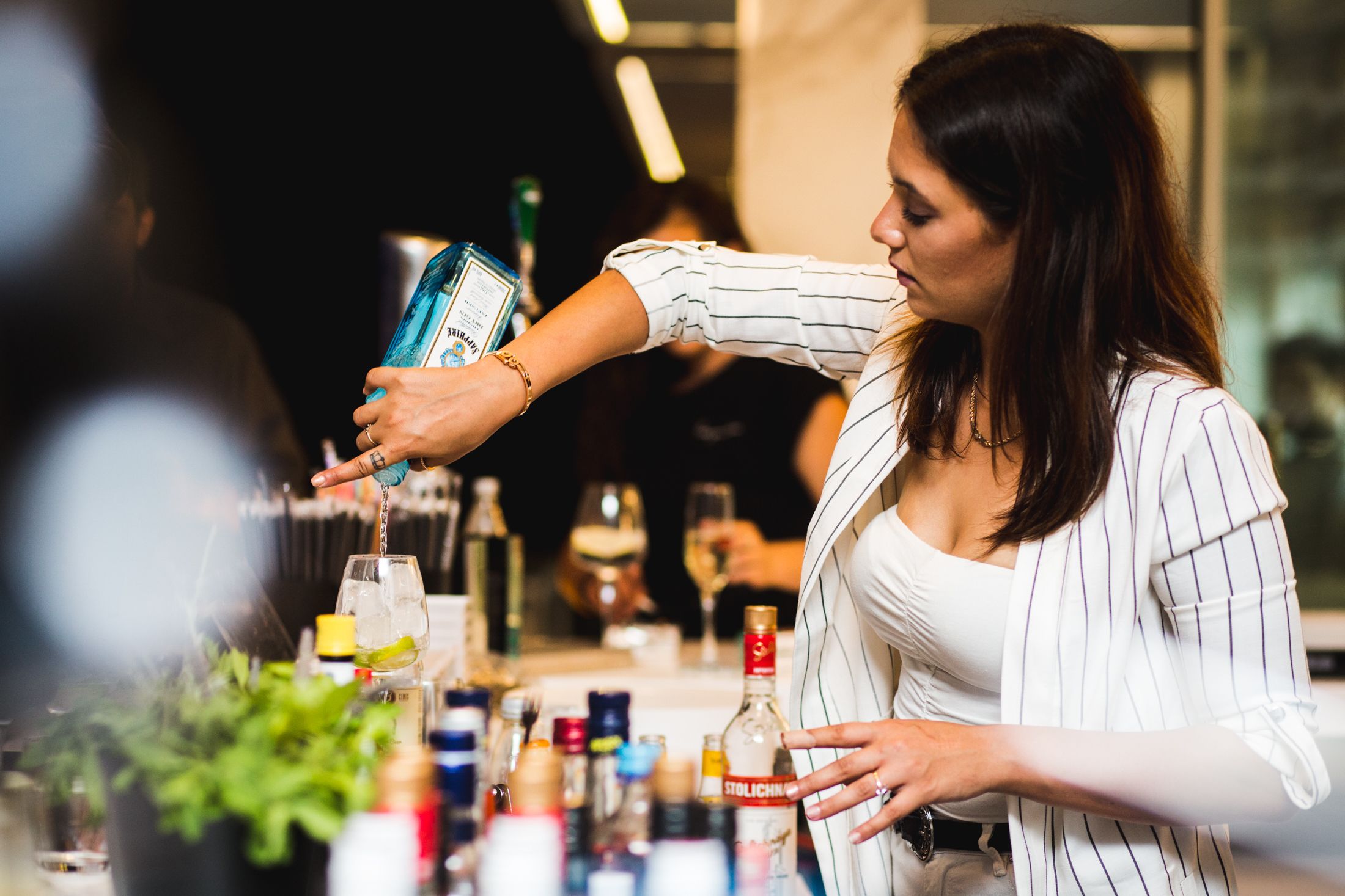 A person pouring a drink at a bar with various bottles and glasses.