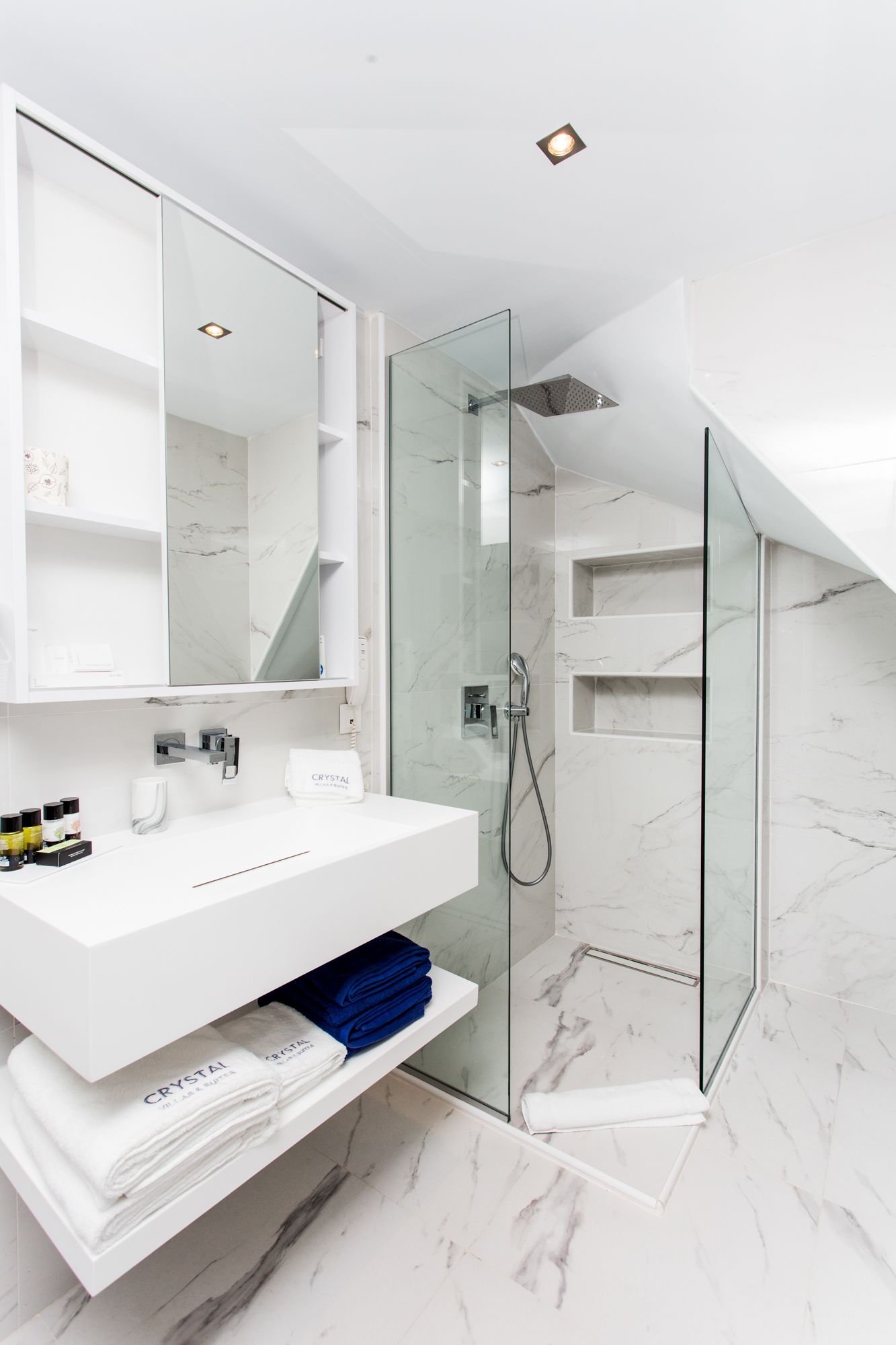 A modern bathroom with a glass-enclosed shower, white marble walls, and a white vanity with a mirror.