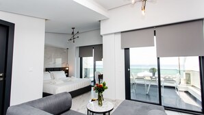 A modern hotel room with a large bed, a sofa, a small table with a vase of flowers, and a balcony with a view of the sea. - Crystal villas & suites (Kassandra)
