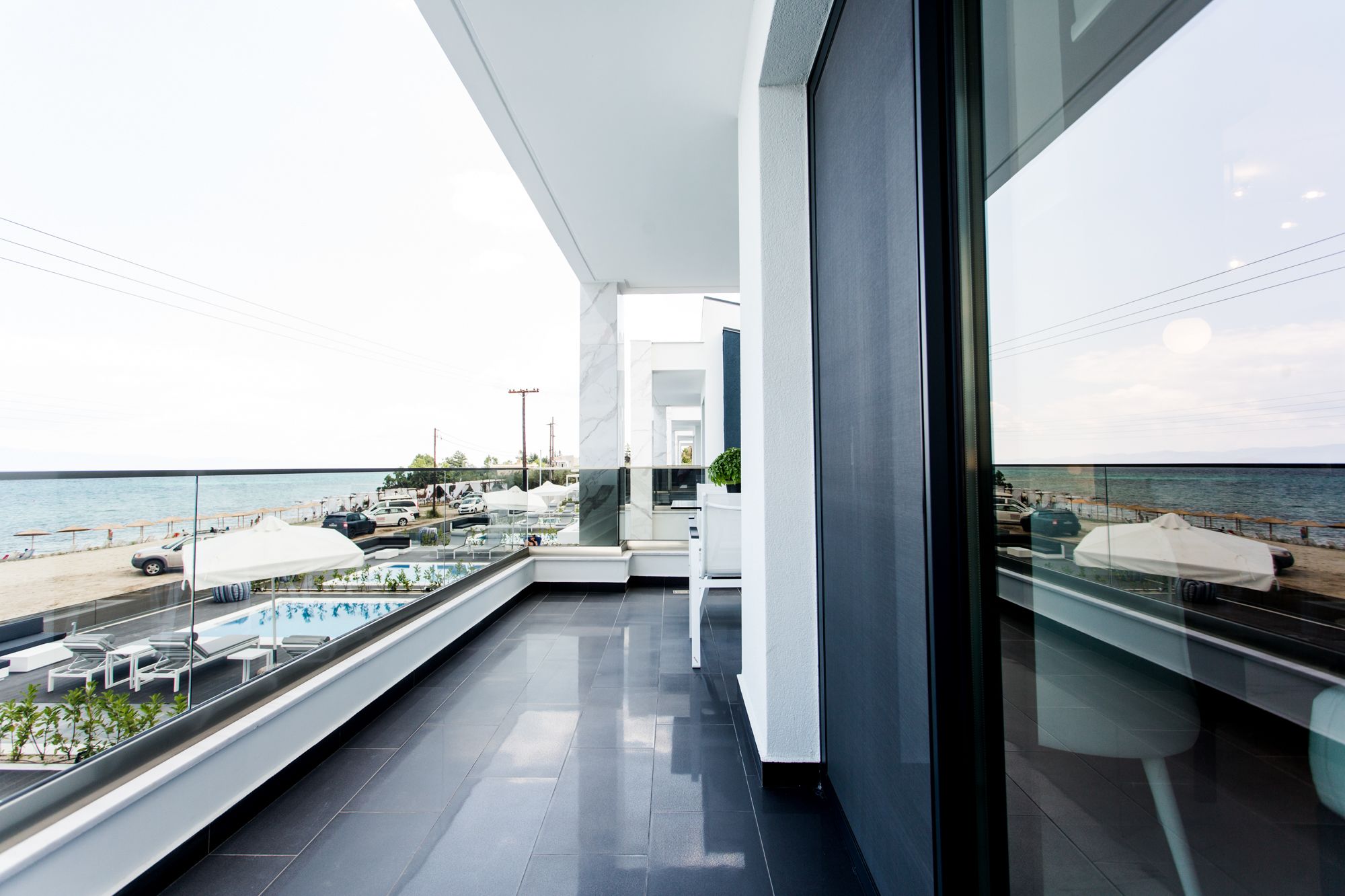A modern balcony with a view of the sea, featuring a pool area and outdoor seating.