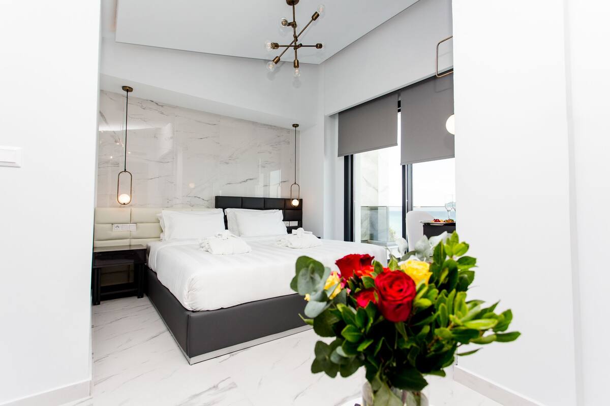 A modern bedroom with a large bed, a marble wall, and a view of the sea.