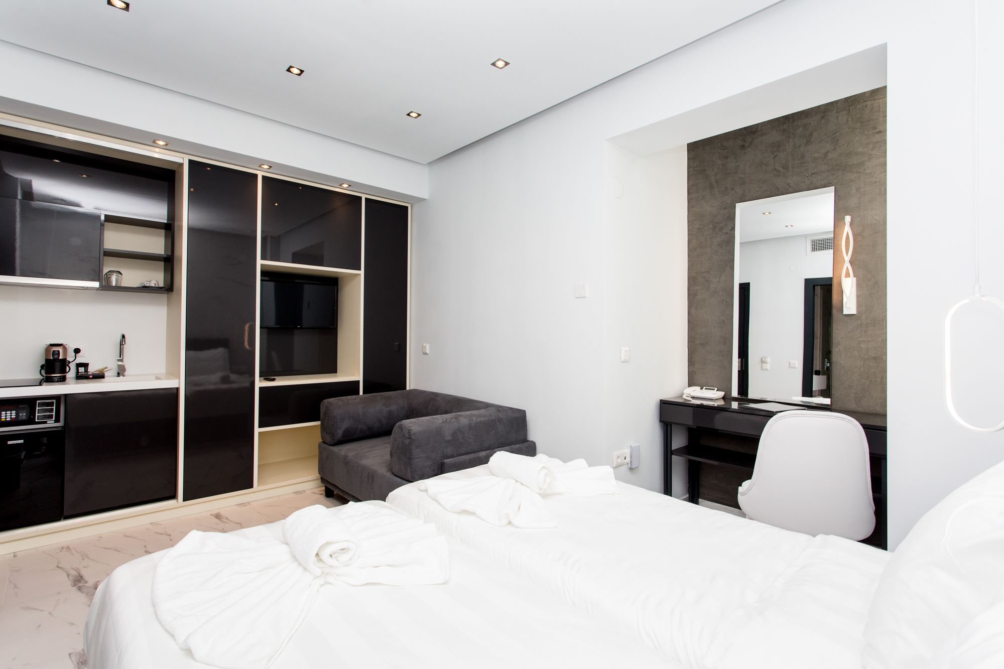 A modern hotel room with a bed, a desk, a chair, a wardrobe, and a television.