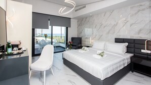 A modern hotel room with a large bed, a desk, and a chair. There is a view of the sea through the window. - Crystal villas & suites (Kassandra)