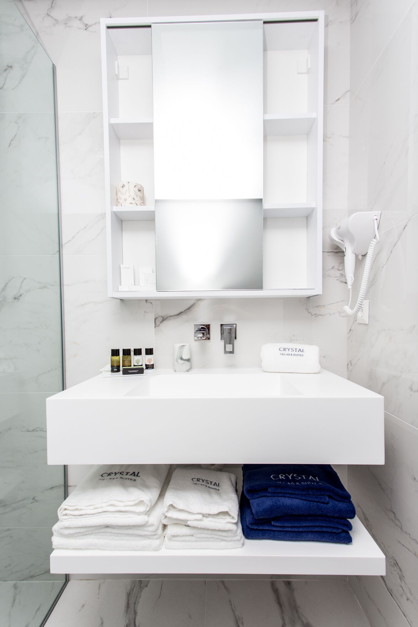 Une salle de bain moderne avec un meuble-lavabo blanc, un grand miroir et un sèche-cheveux fixé au mur.