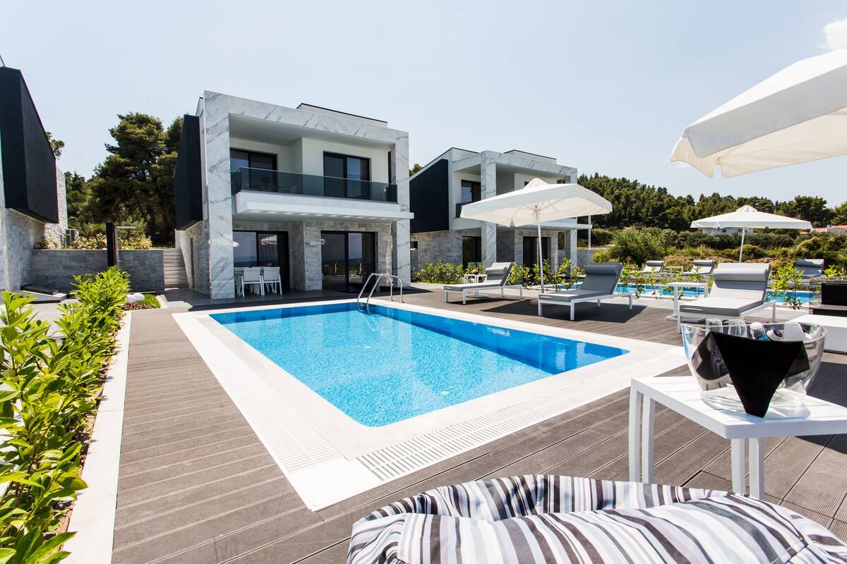 A modern outdoor pool area with a rectangular pool, lounge chairs, and umbrellas.