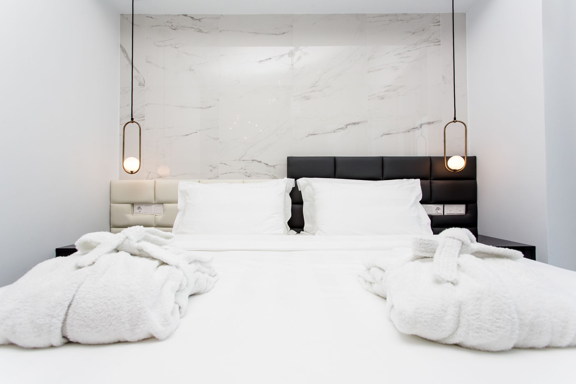 Habitación de hotel moderna con pared de diseño de mármol, cabecera negra y dos lámparas de noche.