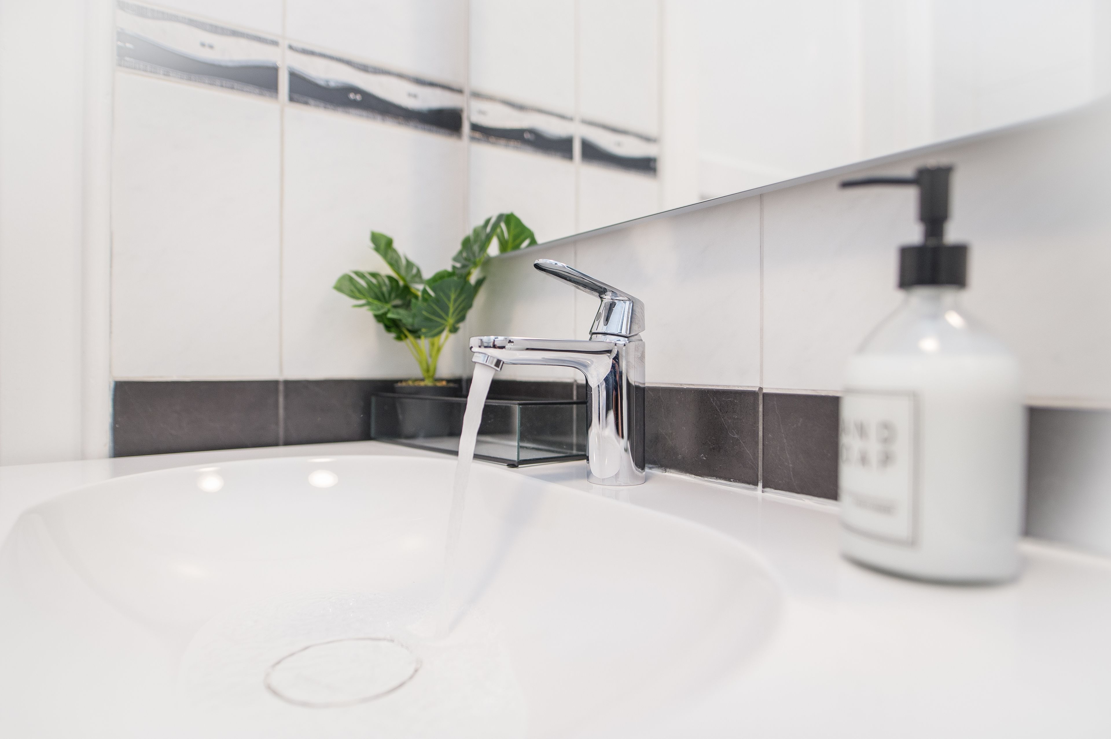 A modern bathroom with a white sink, chrome faucet, and a soap dispenser.