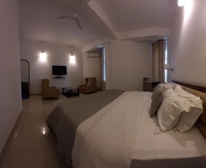 A hotel room with a large bed, two armchairs, a small table, a TV, and a ceiling fan. - Hotel Saramati (Dimapur)