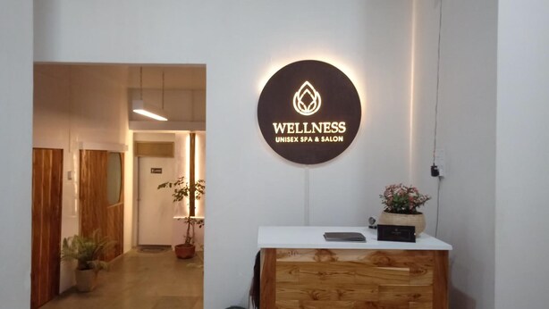 A reception area with a wooden reception desk, a sign reading "WELLNESS UNISEX SPA & SALON", and a potted plant. - Hotel Saramati (Dimapur)