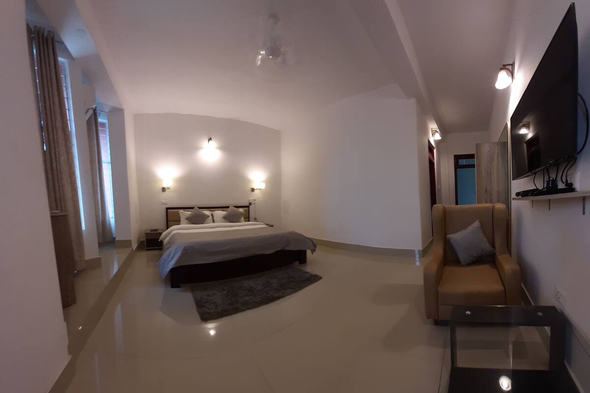 Une chambre moderne avec un lit, un canapé, un téléviseur et un téléviseur à écran plat fixé au mur.