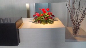 A reception desk with a vase of red flowers, a black box, and a decorative branch on the right. - Hotel Saramati (Dimapur)