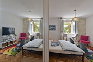 A modern bedroom with a bed, a TV, a desk, and a chair. There are windows with curtains, a bookshelf, and a plant. - Harmony Room Hvar (Hvar)