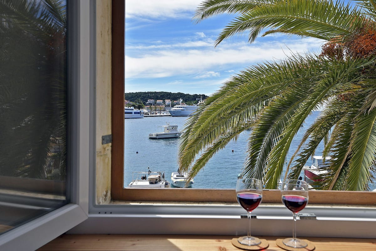 A view from a window overlooking a marina with boats, palm trees, and a distant town.