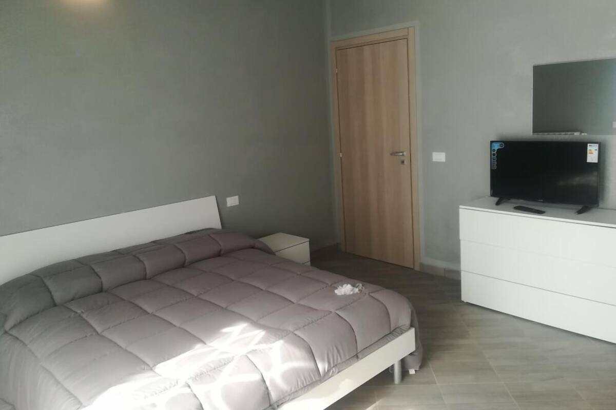 Un dormitorio con una cama, un televisor sobre una cómoda y una puerta de madera.