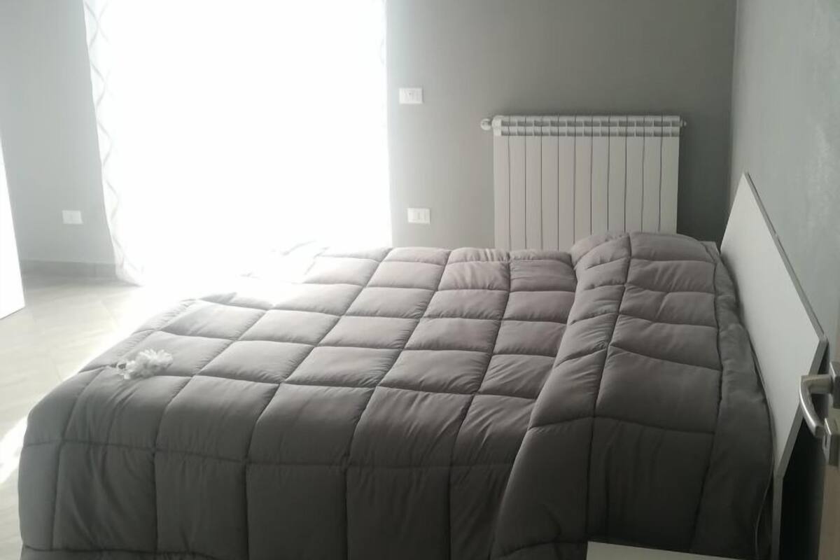 Un dormitorio con cama, radiador y ventana con cortinas.