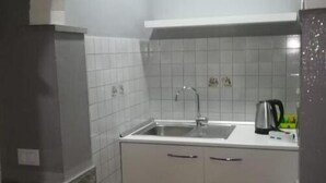 Una cocina compacta con armarios blancos, un lavabo y un hervidor.