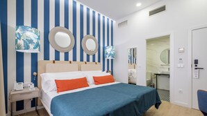 Ένα δωμάτιο ξενοδοχείου με ένα κρεβάτι, ένα κομοδίνο, έναν καθρέφτη και ένα μπάνιο που φαίνεται μέσα από μια ανοιχτή πόρτα.
