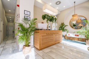 A reception desk with a wooden finish, a large mirror, and potted plants. - Soho Boutique Urban (Málaga)