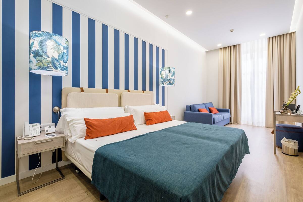 A hotel room with a bed, a desk, a chair, and a sofa.