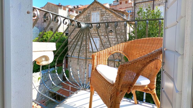 A wicker chair on a balcony with a view of stone buildings and a clear sky. - Historic Piazza House & Romantic Garden (Hvar)
