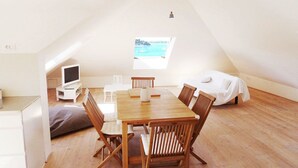 A cozy, well-lit room with a wooden dining table and chairs, a small TV on a white stand, and a window offering a view of the sea. - Hvar Attic Apartment (Hvar)